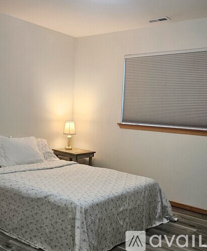A bedroom with a bed, nightstand, and window with blinds.