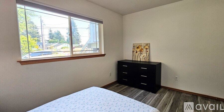 A bedroom with a bed, dresser, and window overlooking a residential area.