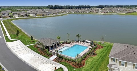 A large swimming pool is surrounded by a grassy area and a few trees.