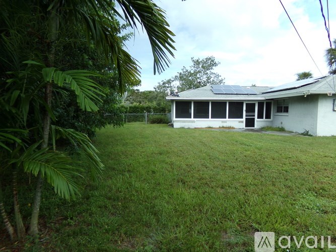 A house with a white exterior and a grey roof is surrounded by greenery.