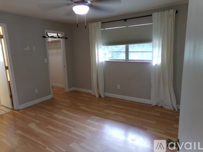 A room with wooden flooring and a window with white curtains.