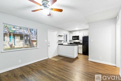A room with a ceiling fan and a kitchen area with a refrigerator and microwave.