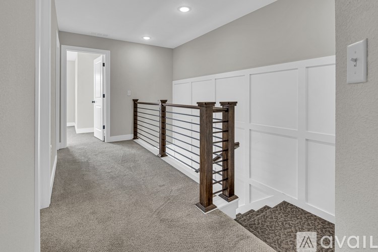 A hallway with a carpeted floor, a staircase with a wooden railing, and white walls.
