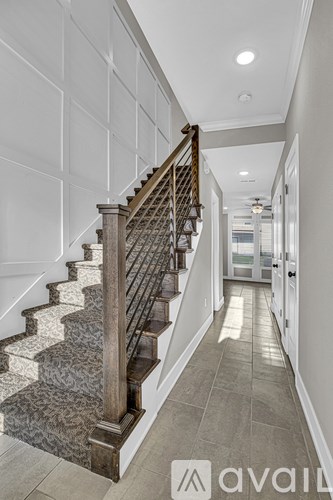 A staircase with a wooden handrail and a marble patterned stair tread leads to a brightly lit hallway.
