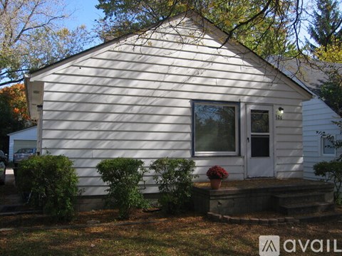 A small white house with a porch and a tree in front.