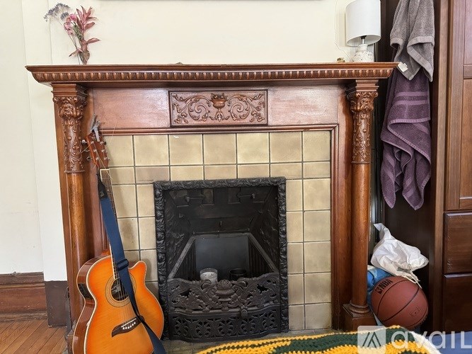 A guitar sits in front of a fireplace with a basketball and a bag on the hearth.