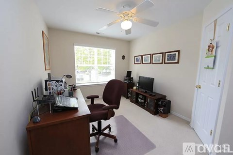 A room with a desk, chair, and a fan.
