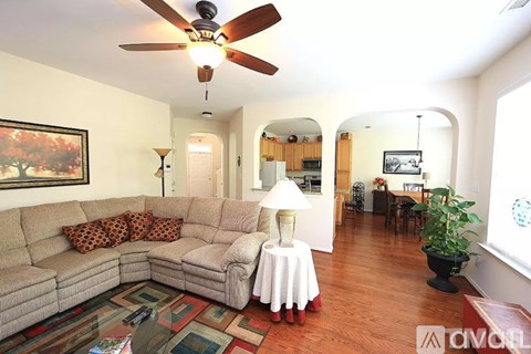 A living room with a couch, a fan, and a painting on the wall.