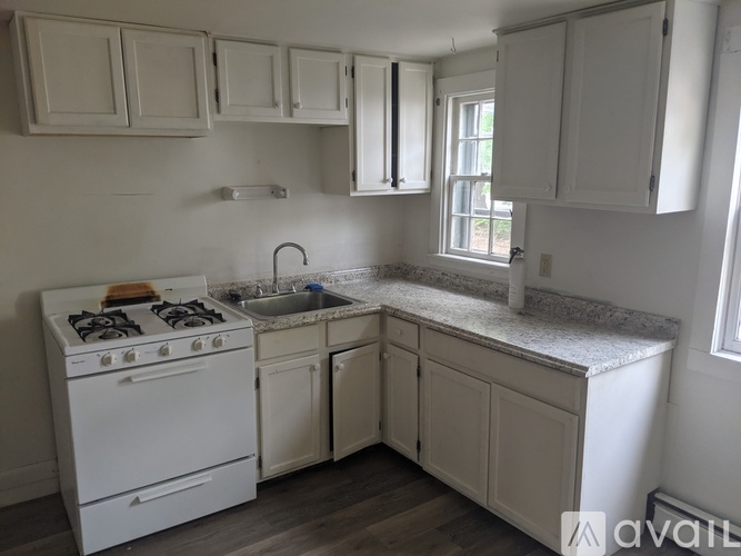 A kitchen with a white stove, cabinets, and a window.