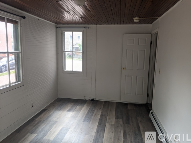 A room with a wooden ceiling and grey flooring with a white door and window.