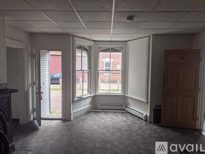 A room with a carpeted floor, a window with blinds, and a door leading to a balcony.