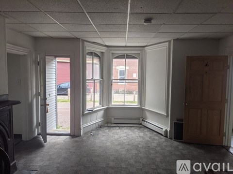 A room with a carpeted floor, a window with blinds, and a door leading to a balcony.