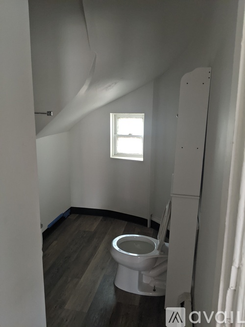 A white toilet in a small room with wood flooring and a window.