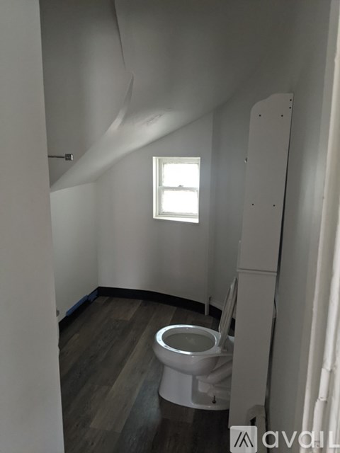 A white toilet in a small room with wood flooring and a window.