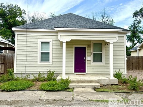 A small house with a purple door is surrounded by a small garden.