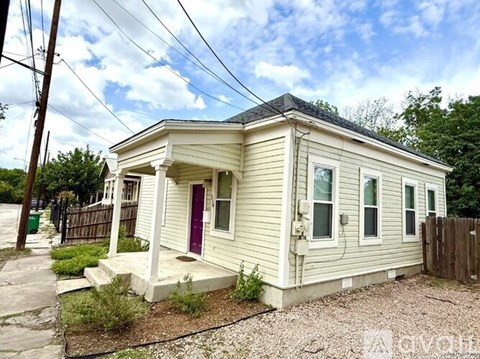 A small white house with a red door is situated in a residential area.