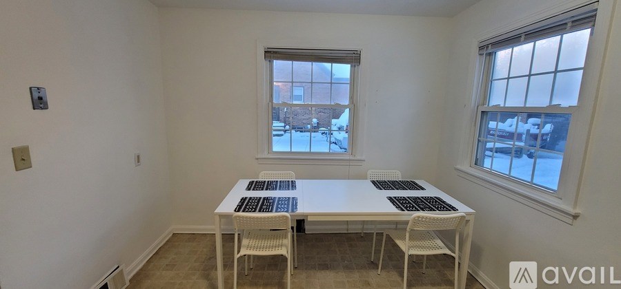 A white table with four chairs is in a room with two windows.