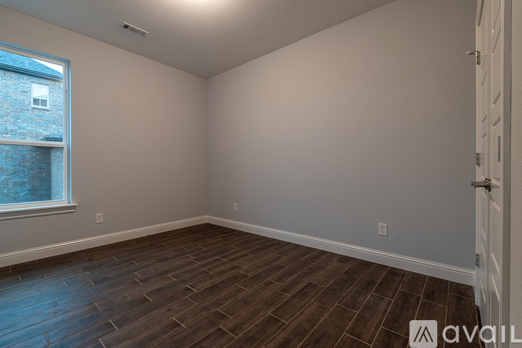 A room with wooden flooring and a window overlooking a brick building.