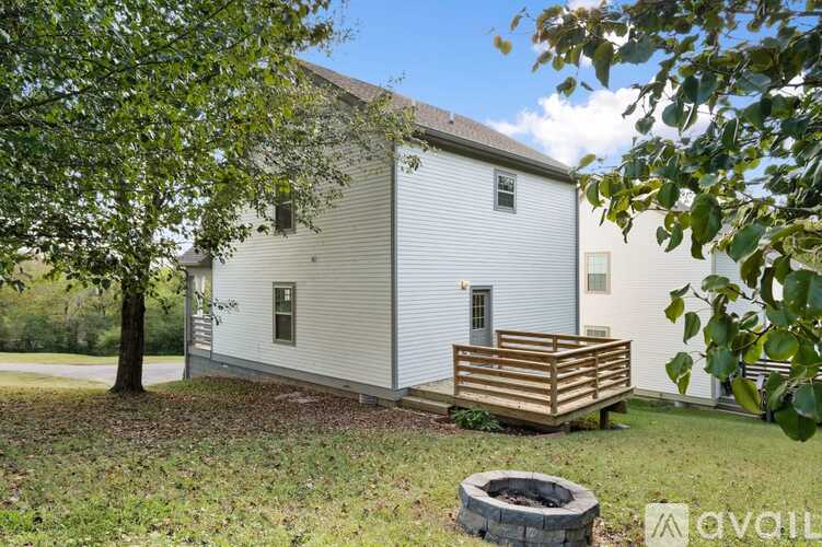 A white house with a wooden deck and a tree in front.