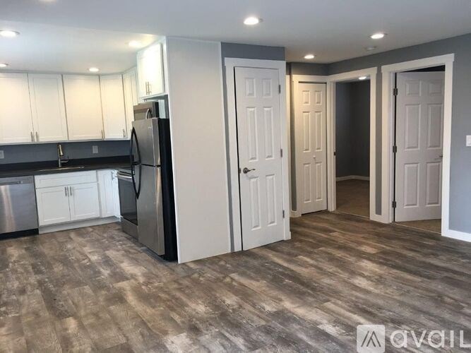 A kitchen with a refrigerator, cabinets, and a wooden floor.