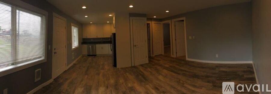 A spacious room with wood flooring and a large window on the left side.