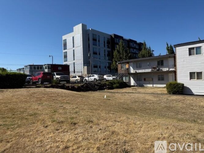 A grassy field with a white building and a red car in the background.