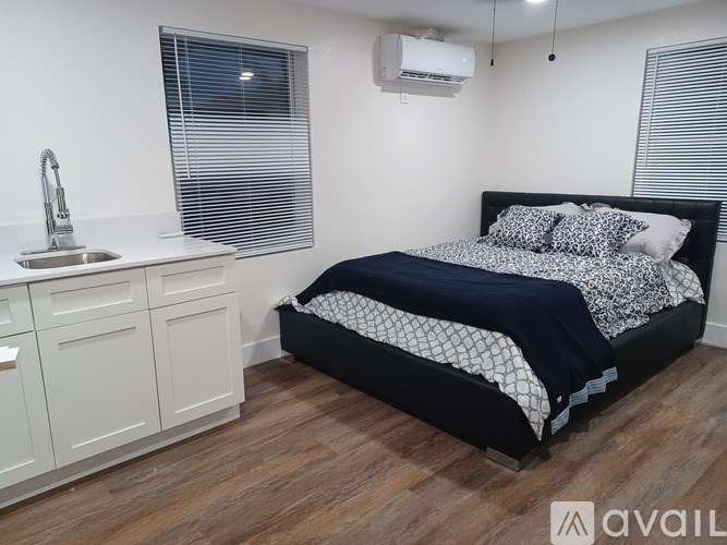 A bedroom with a bed, sink, and cabinets.