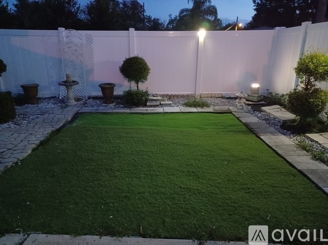 A backyard with a green lawn and a white fence.