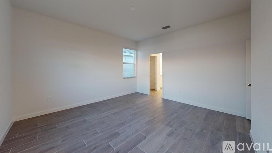 A room with wooden flooring and a door leading to another room.