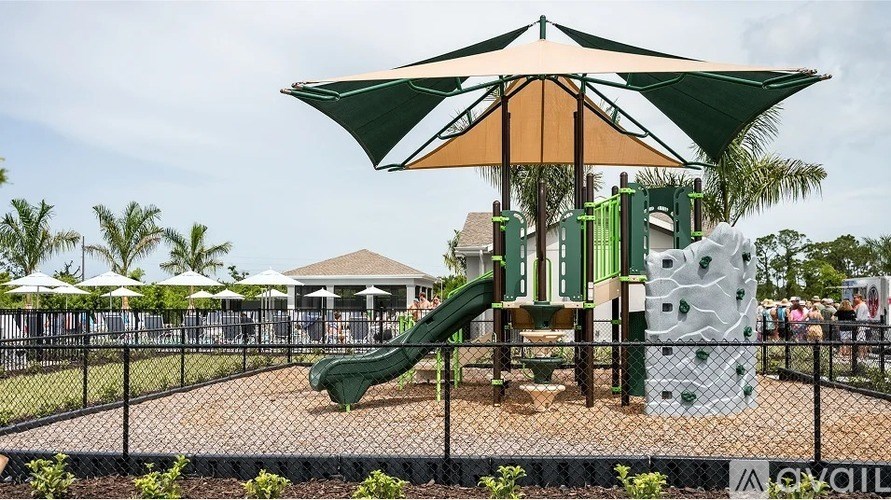 A playground with a green slide and a large umbrella.
