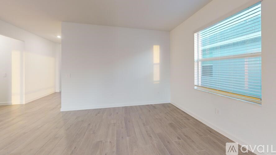 A spacious room with wooden flooring and a window with blinds.