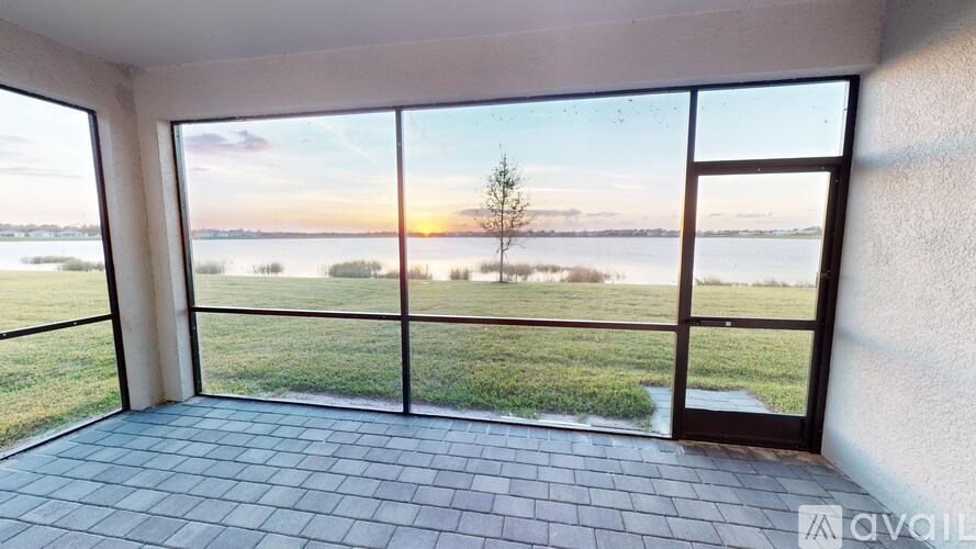 A room with a view of a body of water and a tree at sunset.