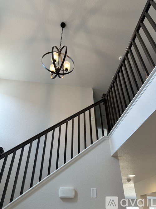A chandelier hangs over a staircase with black railings.