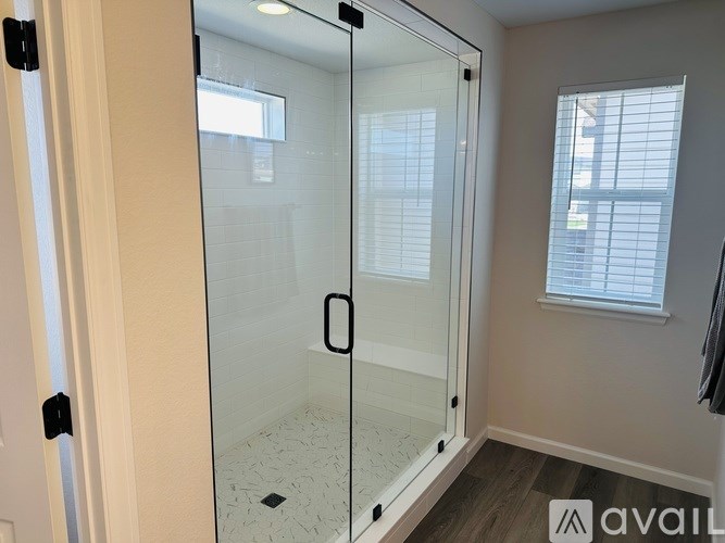 A bathroom with a glass shower door and a window with blinds.