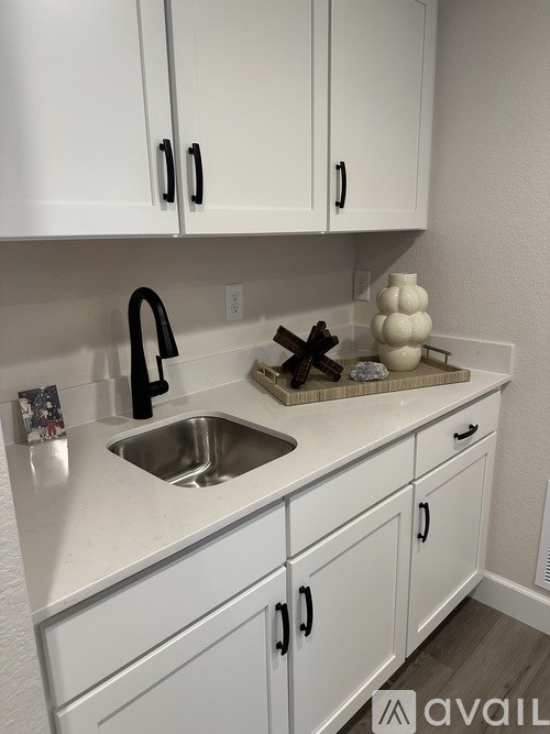A kitchen with white cabinets and a black faucet.