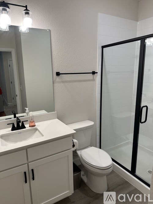 A bathroom with a toilet, sink, mirror, and shower.