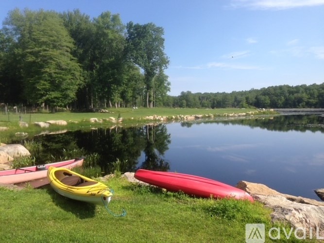 Two kayaks are on the grass by the water.