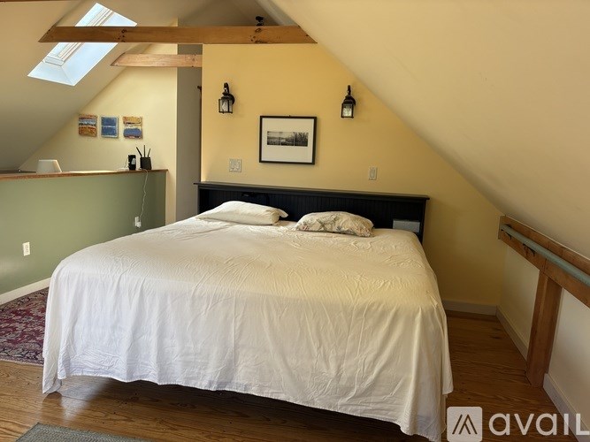 A bedroom with a bed, a skylight, and a picture on the wall.