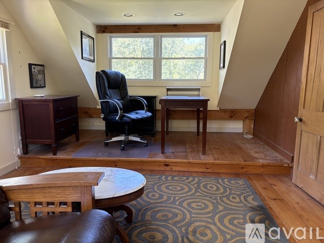 A living room with a brown leather couch, a wooden table, a black office chair, and a wooden cabinet.