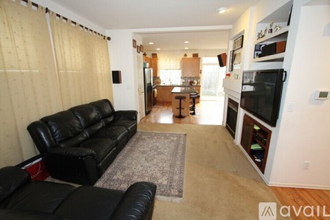 A black leather couch sits in a living room with a rug in front of it.