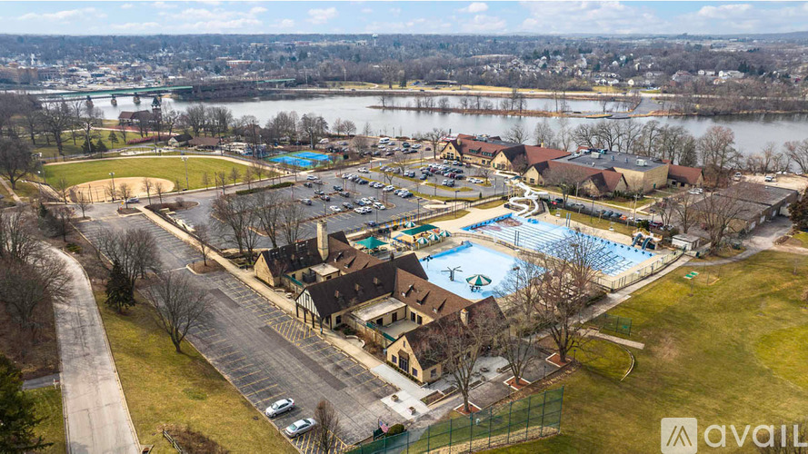 A large outdoor swimming pool surrounded by a grassy area and a parking lot.