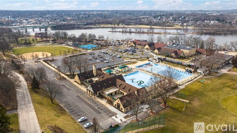A large outdoor swimming pool surrounded by a grassy area and a parking lot.