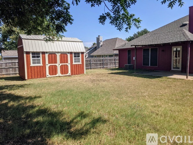 A red shed sits in a grassy yard next to a house.