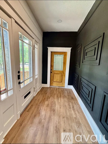 A hallway with a wooden floor, white walls, and a wooden door.