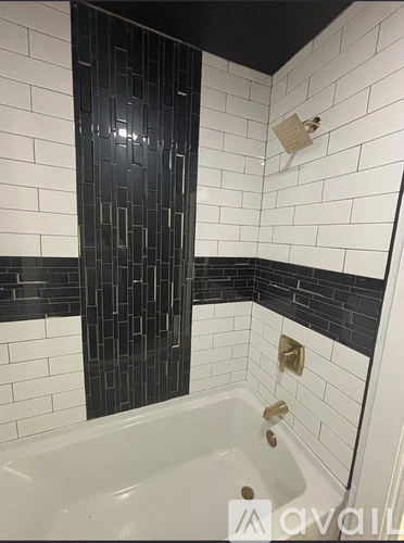A bathroom with a white tub and black and white tiles.