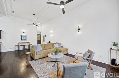 A living room with a beige couch, a grey armchair, a coffee table, and a ceiling fan.