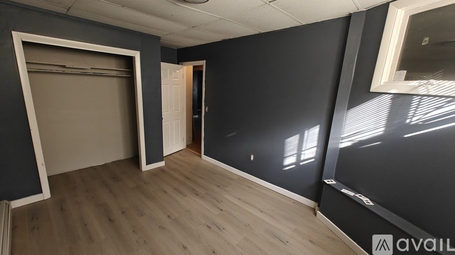 A room with dark walls and wooden flooring, with a large window on the right side.