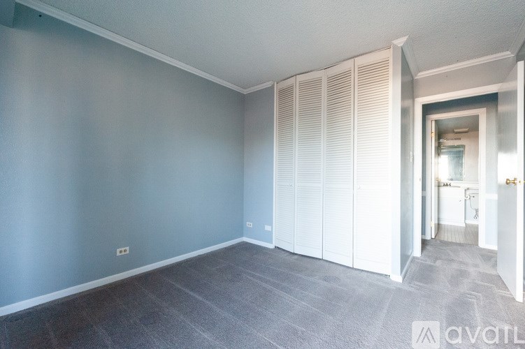 A room with grey carpet and white walls with a doorway leading to another room.