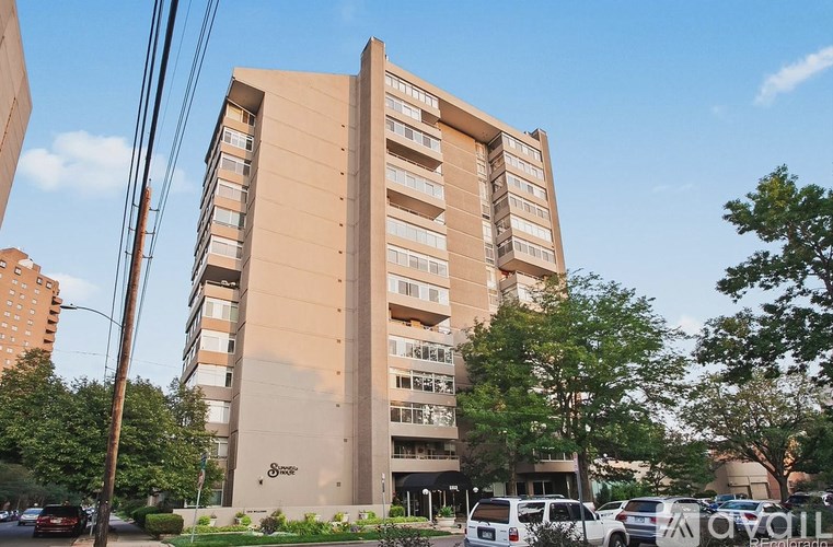 A tall beige building with the word "Sunset" on the side is surrounded by trees and parked cars.
