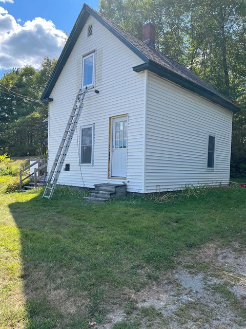 A small white house with a ladder in front.
